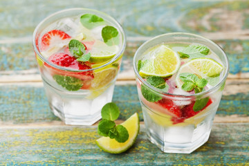 Summer lemonade or cocktail with lime, ice, strawberry and green mint in glass on rustic wooden...