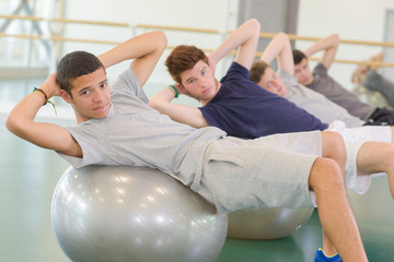 Four men leaning on aerobic balls, twisting towards camera