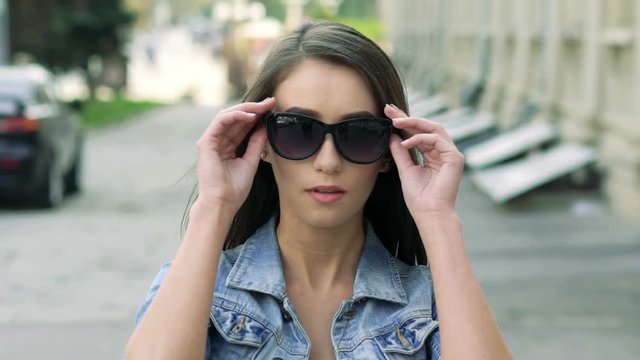 Pretty girl walking on camera and taking off sunglasses. Slowly