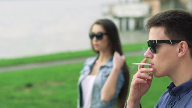 Young man smoking, girl coming and putting hands on him. Slowly