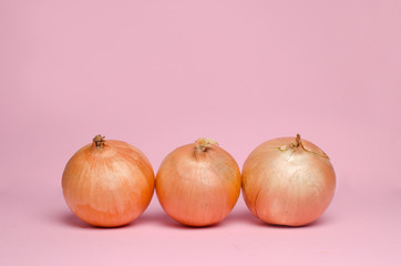 Whole three onions on a pink background