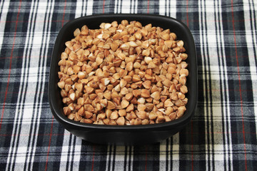 Uncooked buckwheat grain in a black bowl on a tablecloth