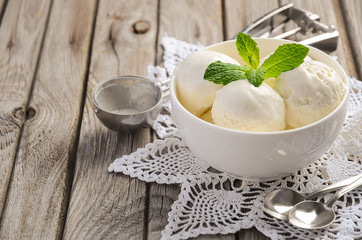 Vanilla ice cream with mint leaves in white bowl on rustic wooden background, selective focus, copy space