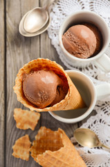 Chocolate ice cream in waffle cone on rustic wooden background, top view