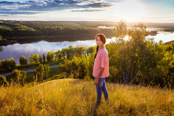 Fototapeta na wymiar Девушка стоит на обрыве, над рекой, в закатном солнце, осень