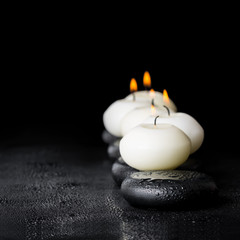 Obraz na płótnie Canvas spa composition of white candles on zen stones with water dew on black background, close up