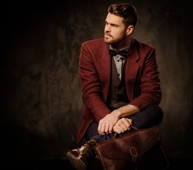 Young handsome old-fashioned man with briefcase posing on dark background.