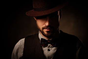 Serious old-fashioned man with hat posing on dark background.