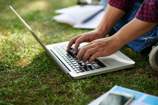 Close-up image of man typing on laptop when sitting on grass