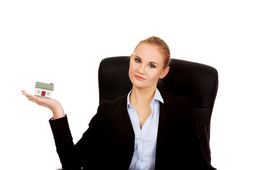 Smiling business woman sitting on a chair and holding house model
