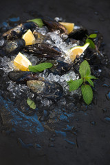 Obraz na płótnie Canvas Fresh uncooked mussels with lemon, herbs and spices on chipped ice over dark slate stone backdrop