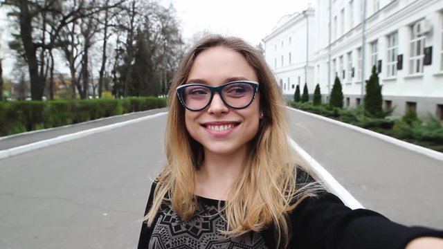 Very Beautiful and Cheerful Girl in the Glasses, Doing Selfie Near the University. Student Hamming and Photographs on Your Phone.