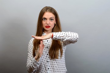 Young woman with a serious face showing time out hand gesture, isolated on grey wall background.