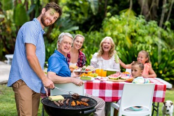 Father grilling food on barbeque in yard 