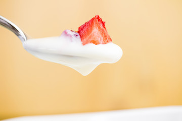 healthy strawberry and white yogurt on the spoon on golden background