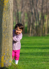 Little girl hiding behind a tree in a forest