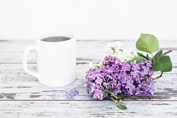 Black tea in white cup on vintage wooden table with branch of lilac 