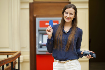 Young happy brunette woman withdrawing money from credit card at
