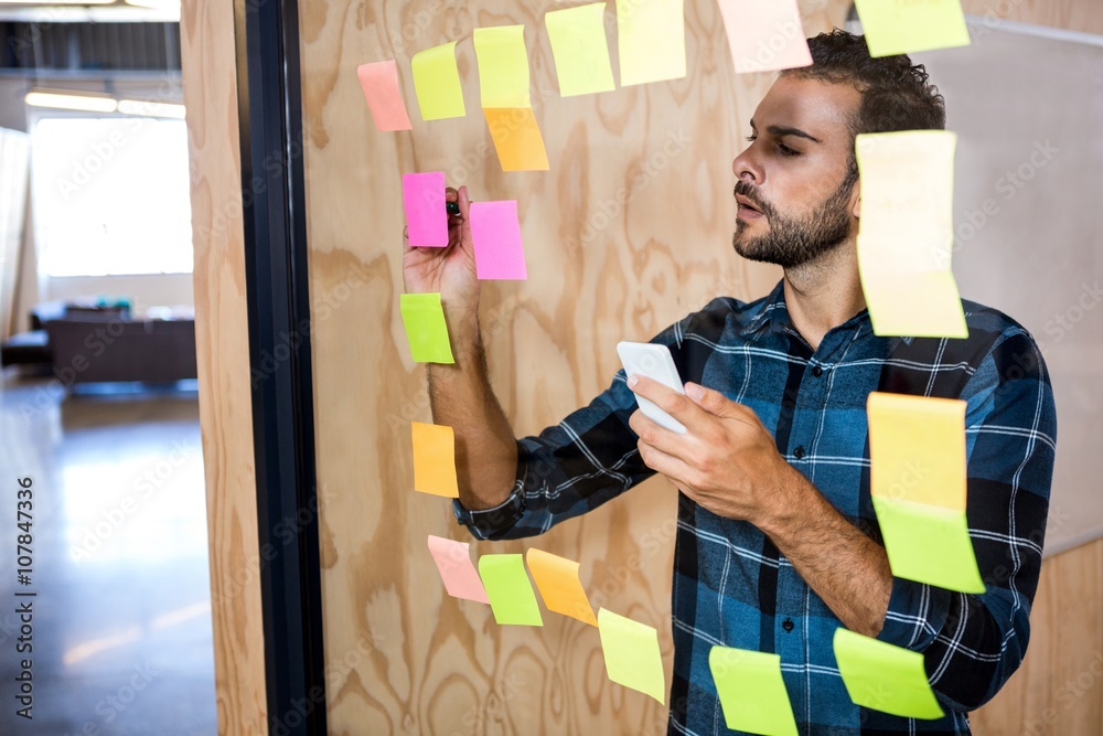 Aufkleber Man using mobile phone while writing on sticky notes 