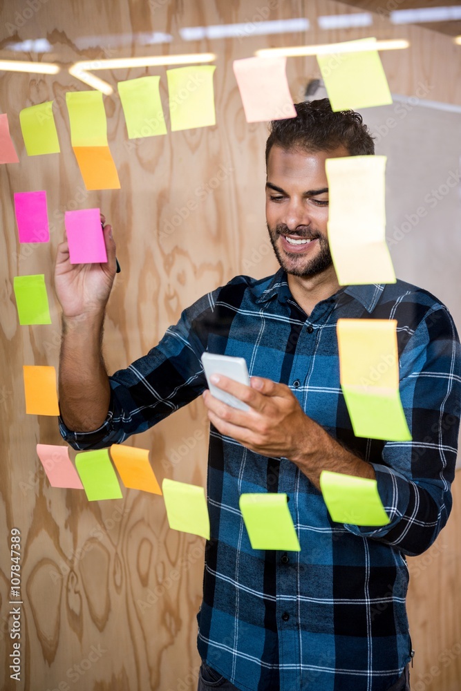 Aufkleber Man using mobile phone while writing on sticky notes 