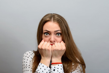 Portrait of a young woman covering her mouth with her fists over grey background. Looking at camera