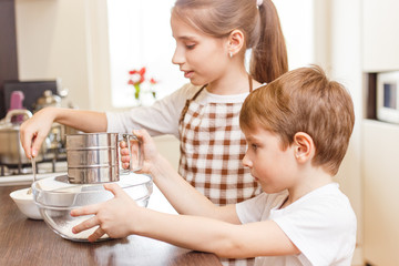 Obraz na płótnie Canvas Small girl with her brother put flour into sieve