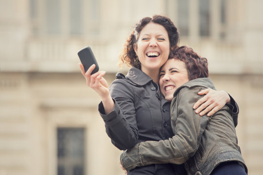 couple of smiling women take selfie in cityscape