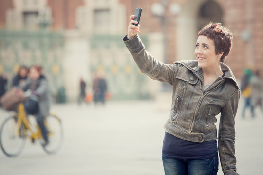 short hair smiling woman take selfie in cityscape