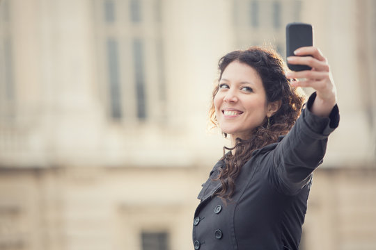 short hair smiling woman take selfie in cityscape