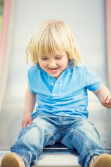 happy smiling blond child play with slide in a park