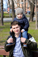 Father and son having fun outdoors on a spring sunny day. Happy smiling little boy in the arms of his dad. Concept of happy family life, love and happiness. 