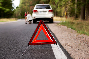 Red warning triangle and broken car in the middle of forrest