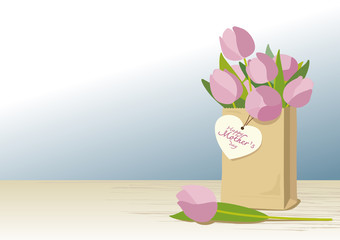 Pink tulips in brown paper bag with mothers day card on wooden floor