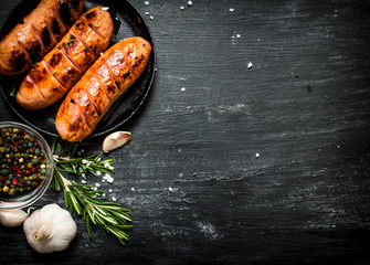 Fried sausages with garlic and herbs in a pan. - obrazy, fototapety, plakaty