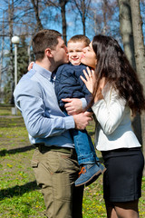 Portrait of happy young family spending time together in green nature in park. Mother, father and son having fun outdoors on a spring sunny day. Concept of happy family life, love and happiness. 