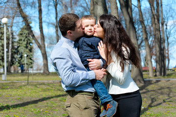 Portrait of happy young family spending time together in green nature in park. Mother, father and son having fun outdoors on a spring sunny day. Concept of happy family life, love and happiness. 