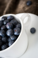 blueberries in a white cup on a brown cloth