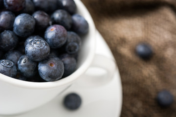 blueberries in a white cup on a brown cloth