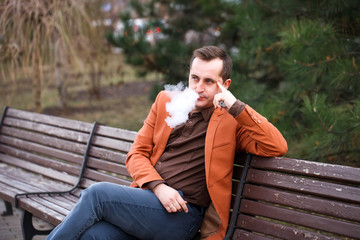 Fototapeta premium A young man sits on a bench and smokes an electronic cigarette.
