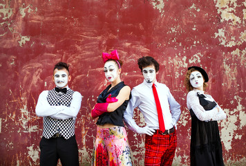 Four mimes standing firmly against the backdrop of a red wall.