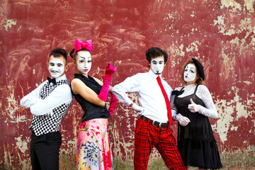 Four mimes standing firmly against the backdrop of a red wall.