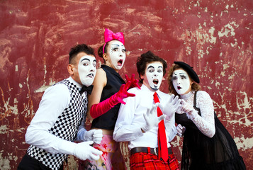 Four mimes in fear stand in the background of a red wall.