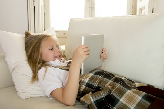 blond little girl lying on home sofa couch using internet app on digital tablet pad on digital tablet pad