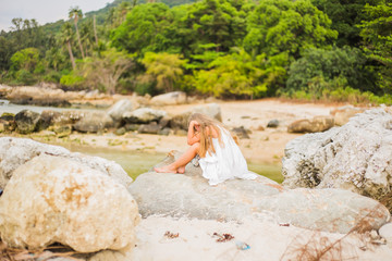 Offended sad girl with long hair sitting on a rock on the shore back

