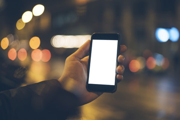 Closeup of male hand holding and using modern smart phone with blank screen for your text or content, with night light bokeh