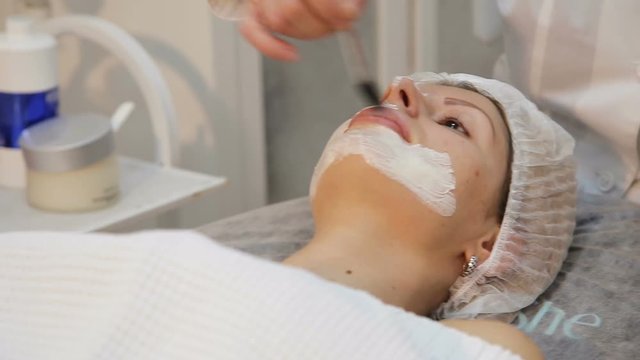 Beautiful woman with facial mask at beauty salon.Applying facial mask at woman face at beauty salon.Spa therapy for young woman receiving facial mask at beauty salon.Beautician does face mask.Spa