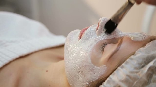 Beautiful woman with facial mask at beauty salon.Applying facial mask at woman face at beauty salon.Spa therapy for young woman receiving facial mask at beauty salon.Beautician does face mask.Spa