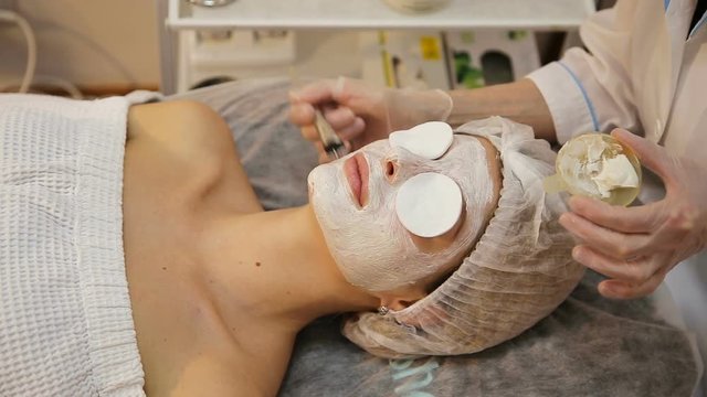 Beautiful woman with facial mask at beauty salon.Applying facial mask at woman face at beauty salon.Spa therapy for young woman receiving facial mask at beauty salon.Beautician does face mask.Spa