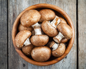 Mushrooms champignons in wooden bowl on table. Top view.