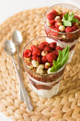 Homemade granola and parfait serverd in high glasses with organic raspberries, nuts and mint. Delicious snack for healthy nutrition.  Breakfast on a straw tablemat with silver spoons.